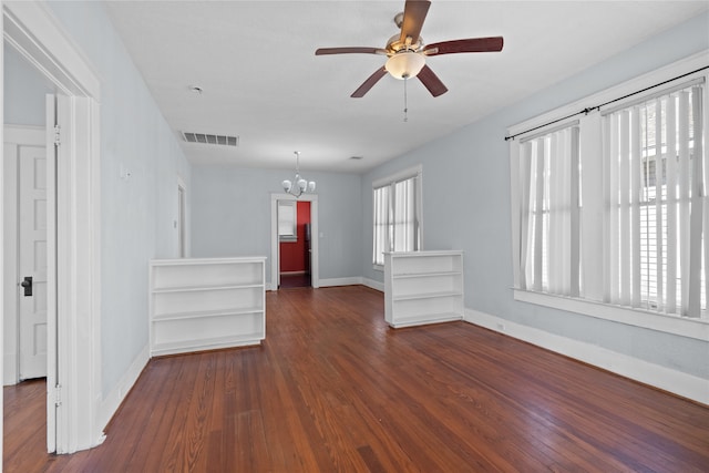 spare room featuring ceiling fan with notable chandelier, a healthy amount of sunlight, and dark hardwood / wood-style flooring