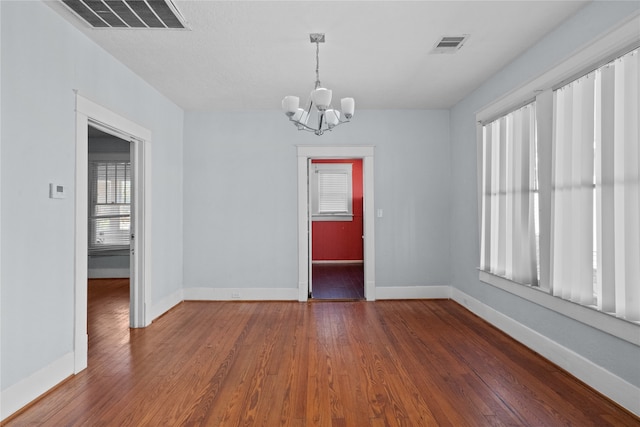 spare room with an inviting chandelier and dark hardwood / wood-style flooring