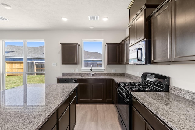 kitchen with light stone counters, black range with gas stovetop, dark brown cabinets, sink, and light hardwood / wood-style floors