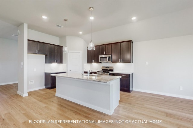 kitchen featuring an island with sink, stainless steel appliances, decorative light fixtures, light stone counters, and sink