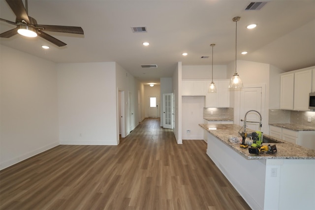 kitchen featuring visible vents, white cabinets, light stone countertops, a kitchen island with sink, and a sink