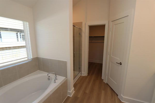 full bathroom featuring a walk in closet, a garden tub, wood finished floors, and a shower stall