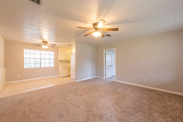 spare room with ceiling fan, a textured ceiling, and light colored carpet