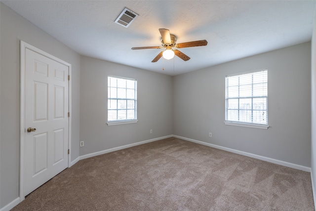 spare room with ceiling fan, a wealth of natural light, and light colored carpet