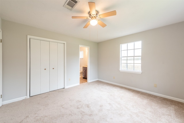 unfurnished bedroom with ensuite bathroom, light colored carpet, a closet, and ceiling fan