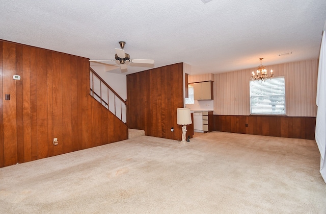 unfurnished living room featuring light carpet, wood walls, a textured ceiling, and ceiling fan with notable chandelier