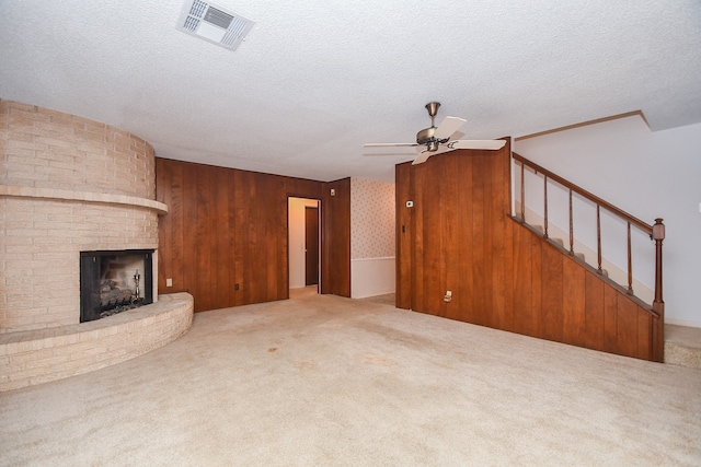 unfurnished living room featuring wood walls, a fireplace, a textured ceiling, light carpet, and ceiling fan