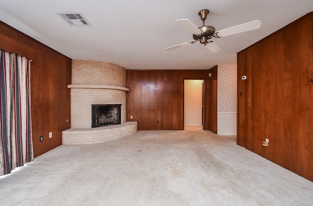 unfurnished living room featuring wooden walls, light colored carpet, a fireplace, and ceiling fan