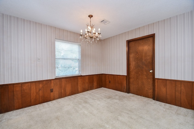 unfurnished room featuring carpet, a notable chandelier, a textured ceiling, and wood walls