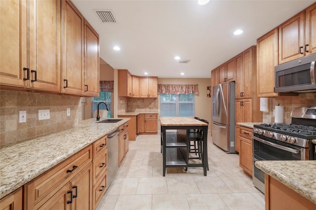 kitchen featuring stainless steel appliances, sink, light stone counters, and backsplash