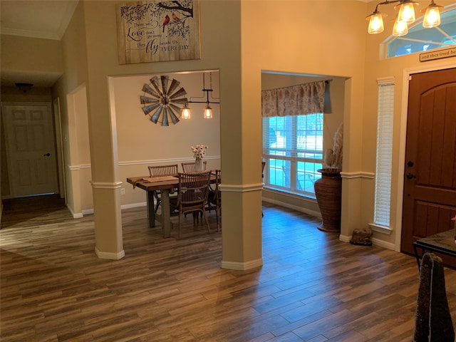 entrance foyer featuring a towering ceiling, decorative columns, dark wood-type flooring, ornamental molding, and an inviting chandelier