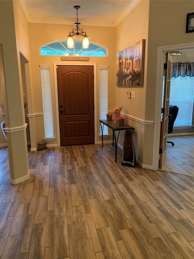 foyer entrance with crown molding, a chandelier, and wood-type flooring