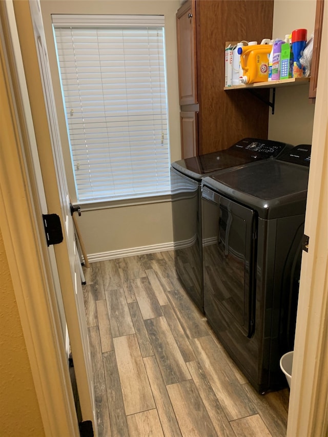 clothes washing area with hardwood / wood-style floors, washer and clothes dryer, and cabinets