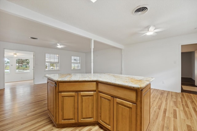 kitchen featuring light wood-style floors, a ceiling fan, visible vents, and light stone counters