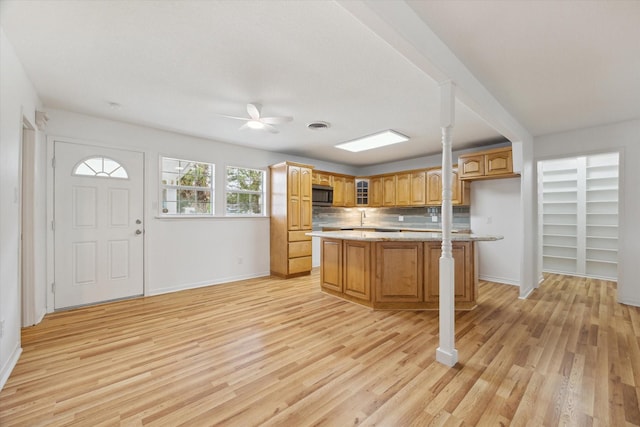 kitchen featuring ceiling fan, light wood-style flooring, a kitchen island, stainless steel microwave, and glass insert cabinets