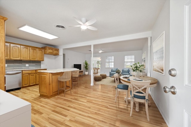 kitchen featuring light countertops, light wood-style flooring, stainless steel dishwasher, open floor plan, and a kitchen breakfast bar