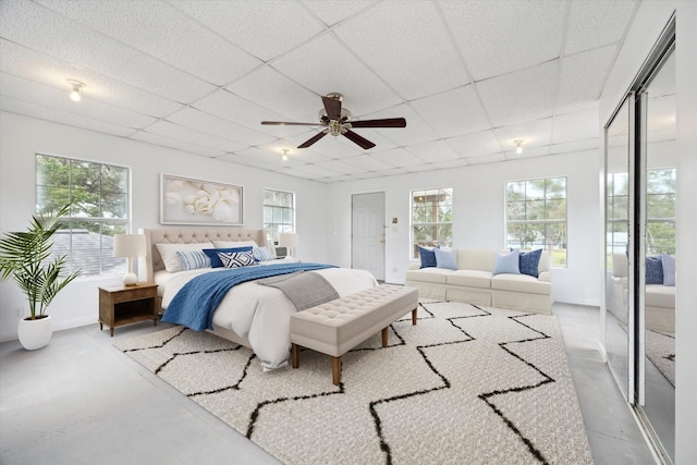 bedroom featuring multiple windows, a drop ceiling, and finished concrete floors