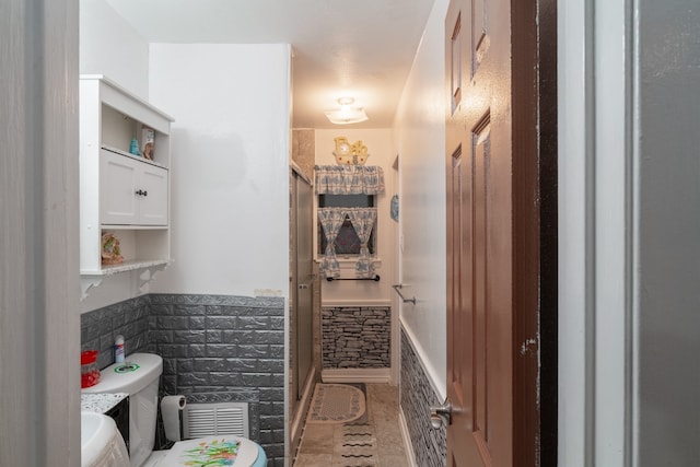 bathroom featuring a shower with door, tile walls, toilet, and tile patterned flooring