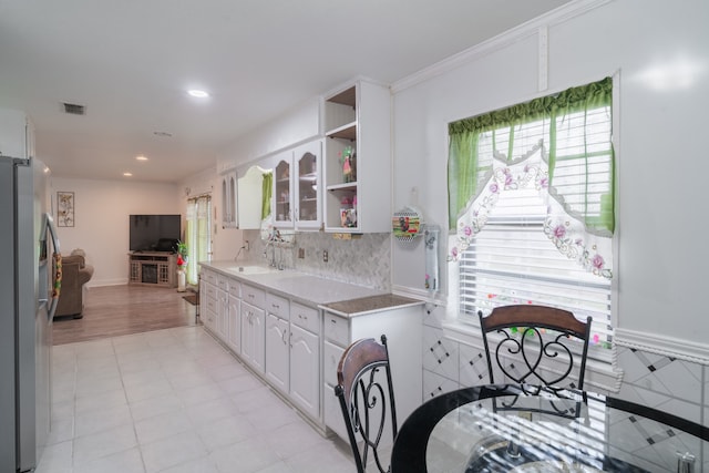 kitchen featuring ornamental molding, white cabinets, plenty of natural light, and stainless steel refrigerator