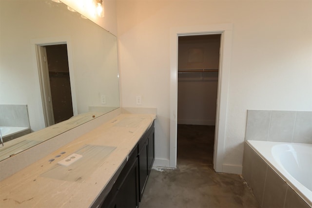 bathroom featuring vanity, a garden tub, a spacious closet, and baseboards