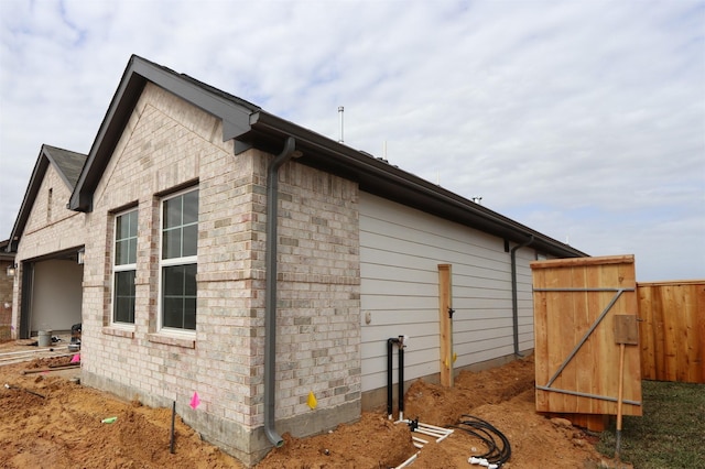 view of side of home featuring brick siding, a gate, and fence