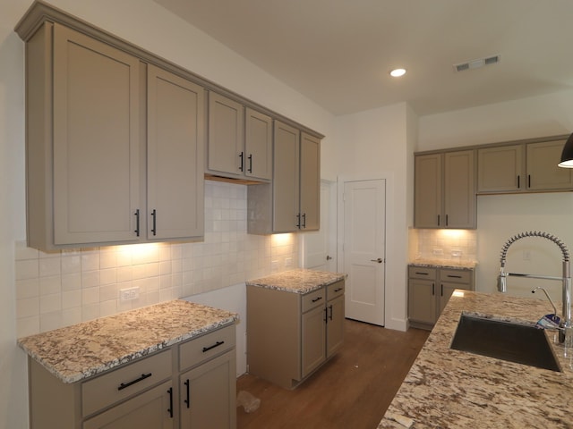 kitchen featuring visible vents, a sink, backsplash, dark wood finished floors, and light stone countertops