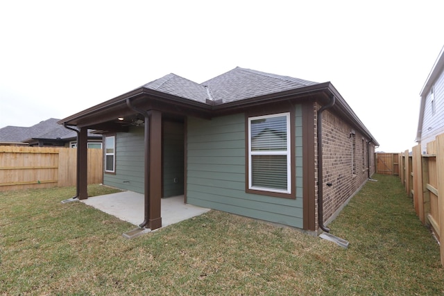 rear view of house with brick siding, a shingled roof, a yard, a fenced backyard, and a patio area