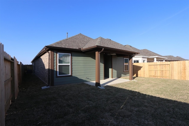 rear view of house featuring a fenced backyard, a yard, and roof with shingles