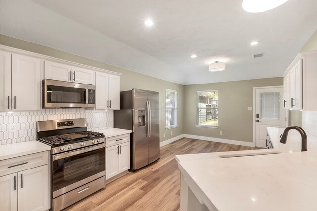 kitchen with light hardwood / wood-style floors, decorative backsplash, white cabinetry, and stainless steel appliances