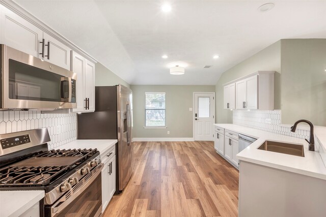 kitchen with tasteful backsplash, appliances with stainless steel finishes, white cabinetry, light hardwood / wood-style flooring, and sink