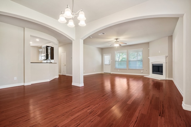 unfurnished living room with ceiling fan with notable chandelier and dark hardwood / wood-style flooring