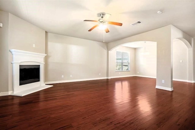 unfurnished living room featuring arched walkways, a fireplace with raised hearth, ceiling fan, wood finished floors, and visible vents