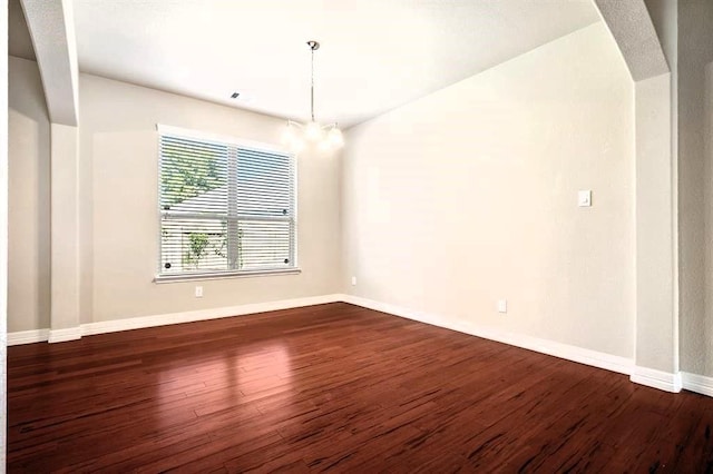 spare room with dark wood-style floors, arched walkways, baseboards, and an inviting chandelier