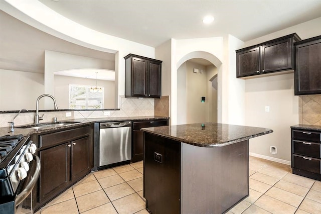 kitchen featuring light tile patterned floors, arched walkways, dark stone counters, stainless steel appliances, and a sink