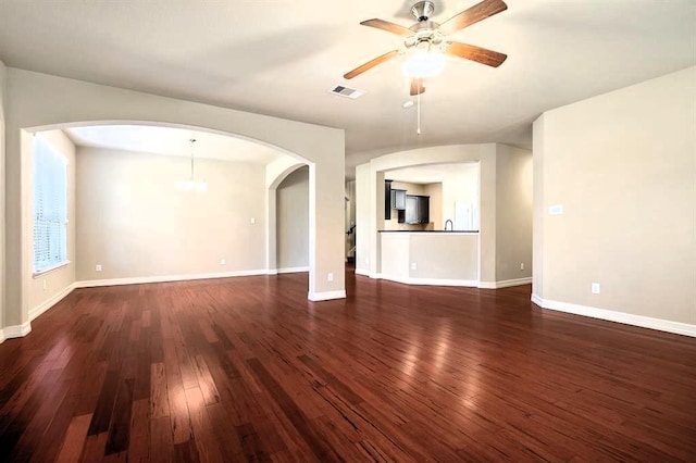 unfurnished living room with dark wood-style floors, baseboards, visible vents, and ceiling fan with notable chandelier