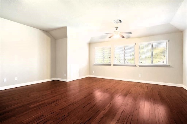 empty room featuring lofted ceiling, dark wood-style flooring, a ceiling fan, visible vents, and baseboards