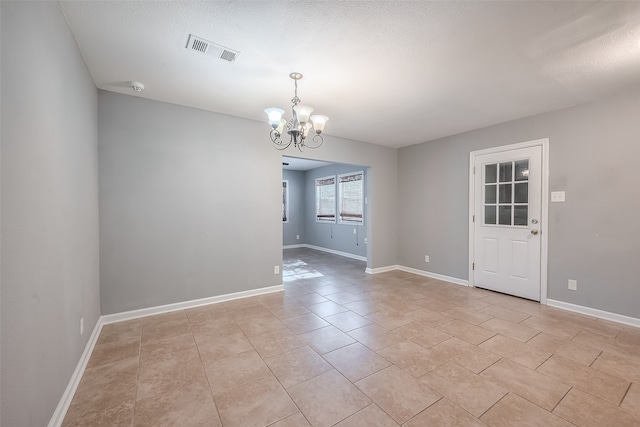 empty room with a chandelier, light tile patterned flooring, and a textured ceiling