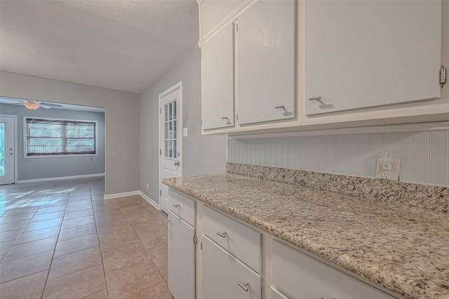 kitchen with light stone countertops, a textured ceiling, ceiling fan, white cabinets, and light tile patterned floors