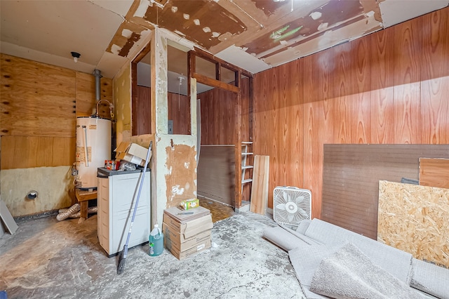 miscellaneous room featuring water heater, concrete floors, and wooden walls