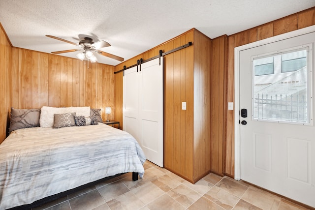 bedroom with ceiling fan, wood walls, a textured ceiling, and a barn door