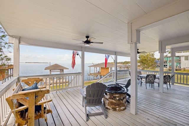 wooden deck with a water view, a fire pit, and ceiling fan