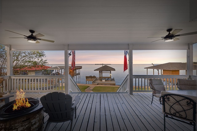 deck at dusk with a water view, a fire pit, and ceiling fan