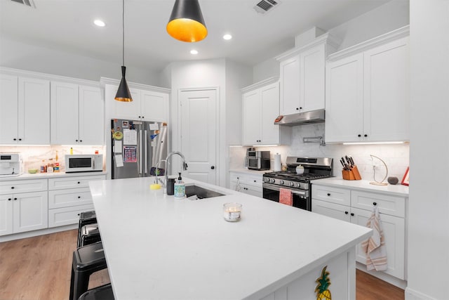 kitchen with white cabinets, stainless steel appliances, hanging light fixtures, and an island with sink