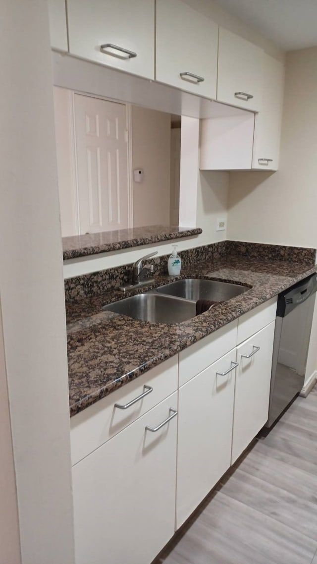 kitchen featuring white cabinets, stainless steel dishwasher, light wood-type flooring, dark stone countertops, and sink