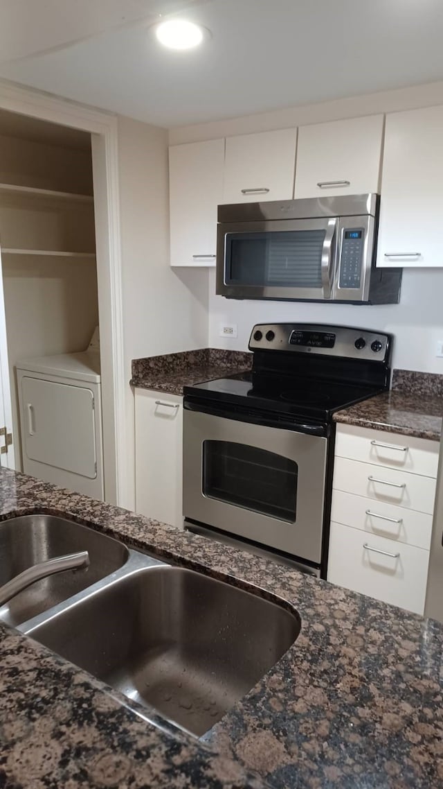 kitchen with white cabinetry, appliances with stainless steel finishes, dark stone counters, and washer / dryer