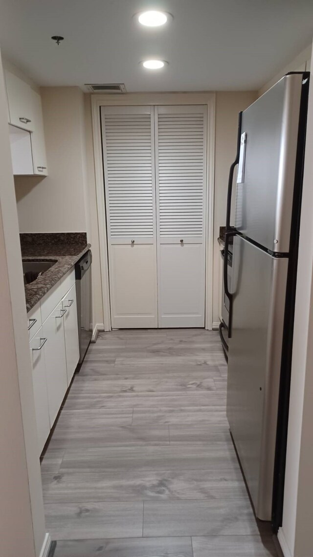 kitchen with dark stone countertops, appliances with stainless steel finishes, light hardwood / wood-style flooring, and white cabinets