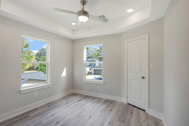 empty room with light hardwood / wood-style flooring, a healthy amount of sunlight, ceiling fan, and a raised ceiling