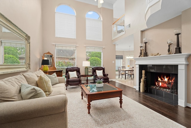 living room with a towering ceiling, dark hardwood / wood-style flooring, and a tiled fireplace