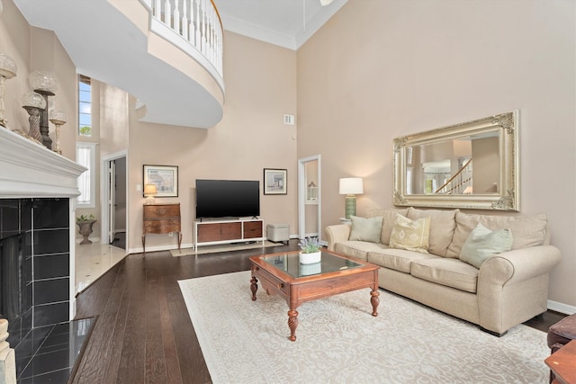 living room with a tiled fireplace, a towering ceiling, wood-type flooring, and crown molding