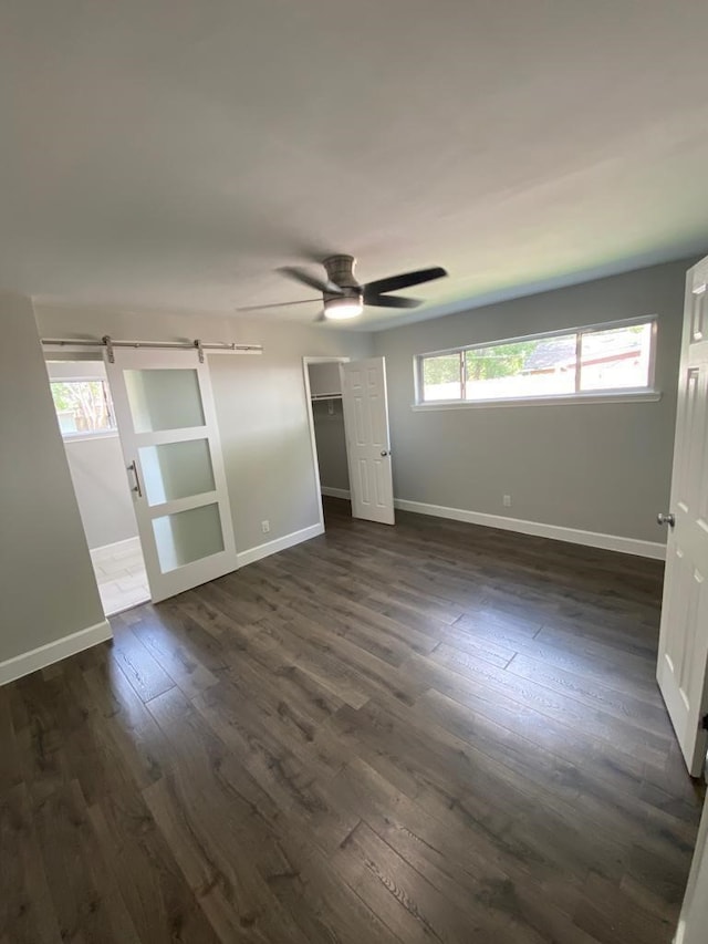 unfurnished room featuring a barn door, dark hardwood / wood-style floors, and ceiling fan